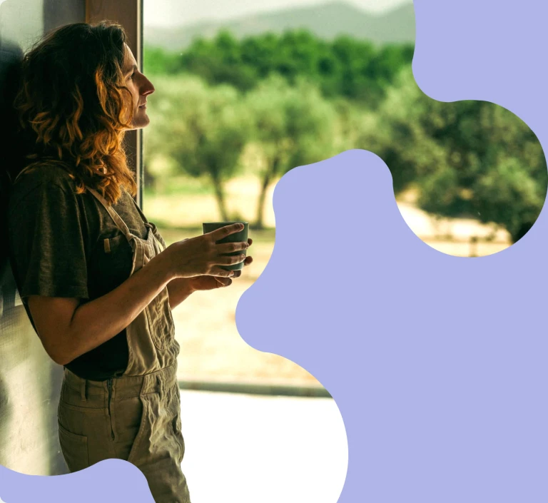 Mujer observando el paisaje a través de una ventana y decidiendo participar de nuestra revolución energética